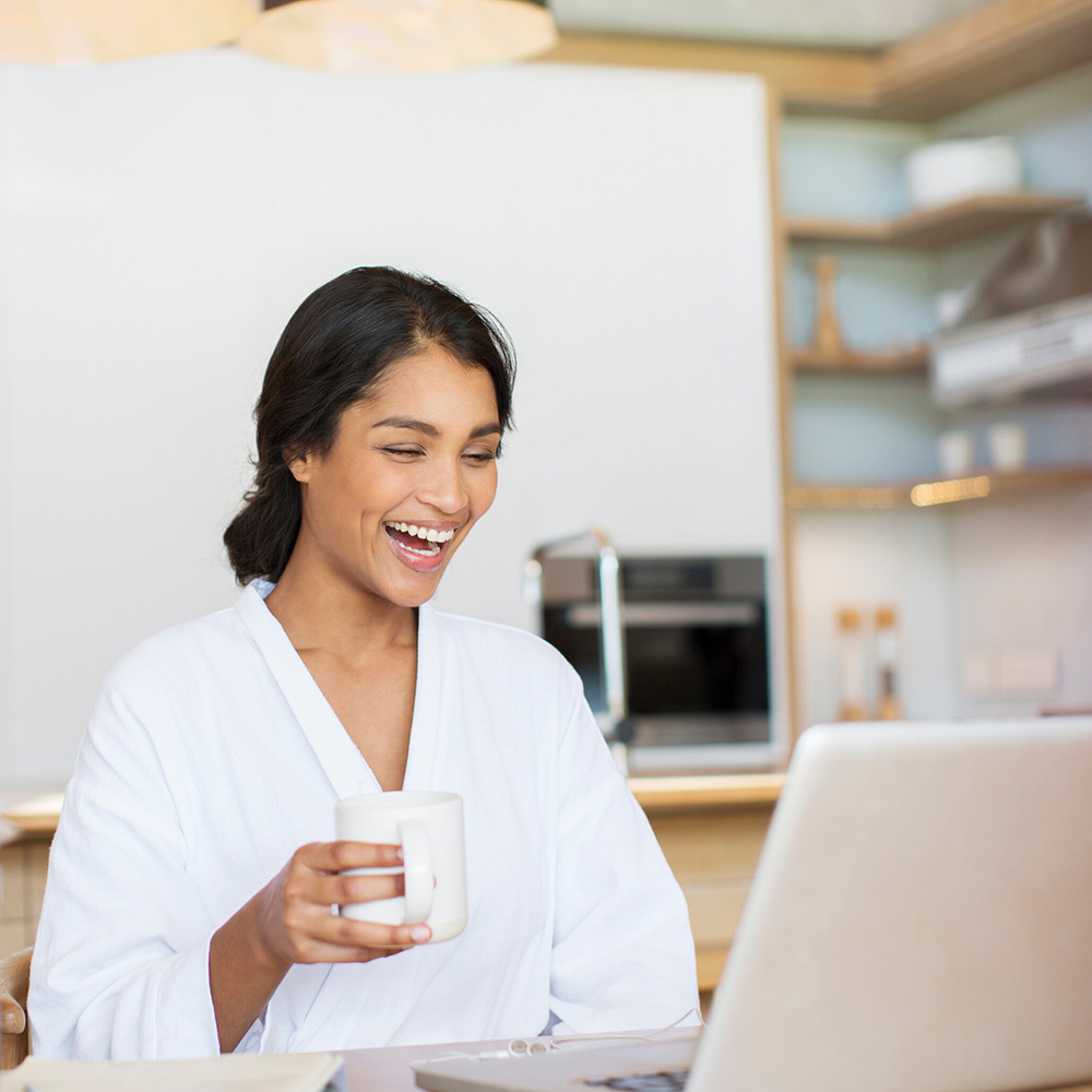 image of woman smiling with coffee in front of computer